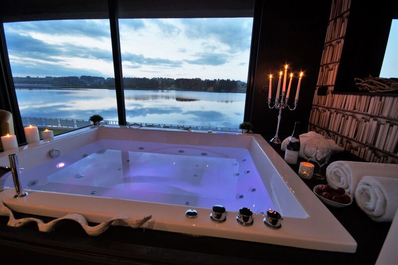 Jacuzzi aux chandelles devant la baie vitrée, avec le lac de Bütgenbach au crépuscule