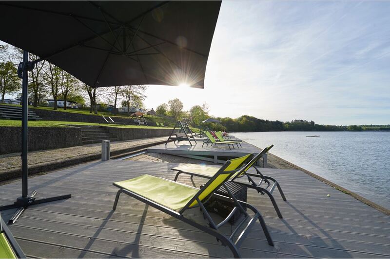 Chaises longues sous un parasol sur une terrasse au bord du lac